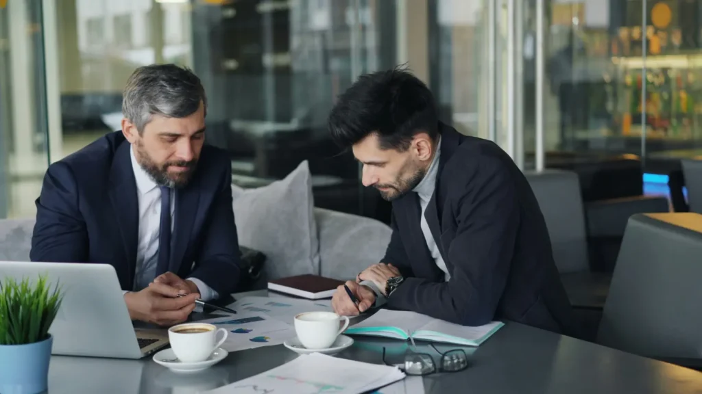 Equipo editorial o consultor financiero trabajando con documentos y portátil en escritorio profesional con expresión seria y concentrada, representando el equipo de especialistas en finanzas y organización de bodas detrás de elweddinghub.es