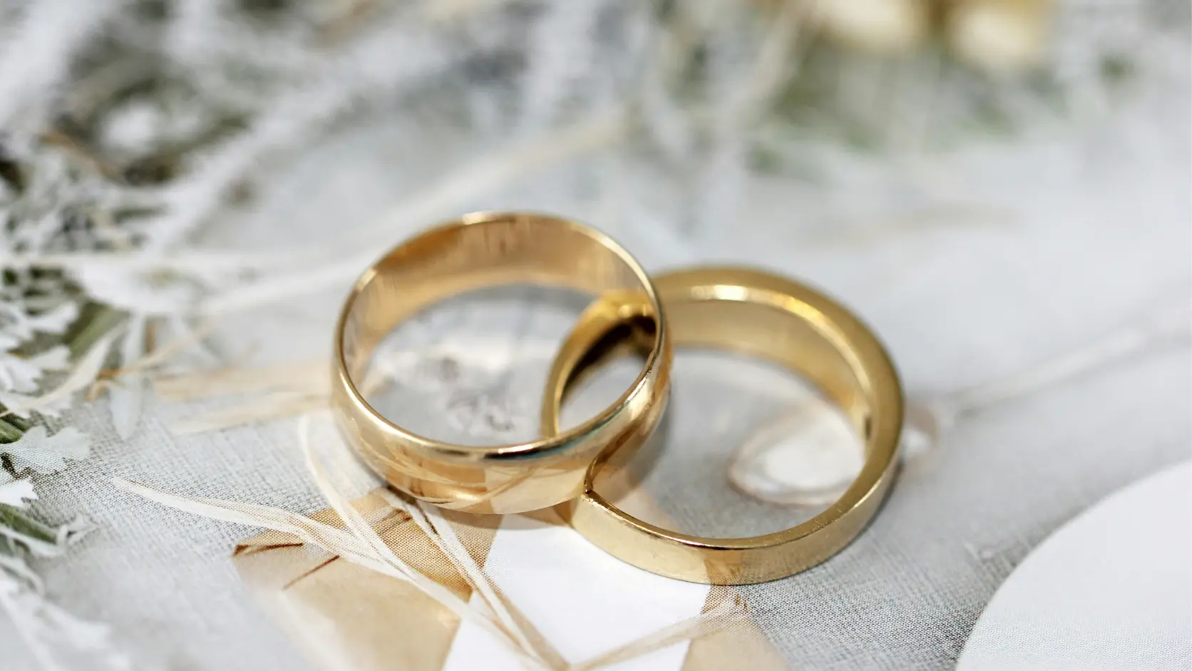 Dos alianzas de boda clásicas de oro colocadas sobre una hoja de cálculo impresa en mármol blanco, representando el control financiero en la compra de alianzas frente a la venta impulsiva de la joyería