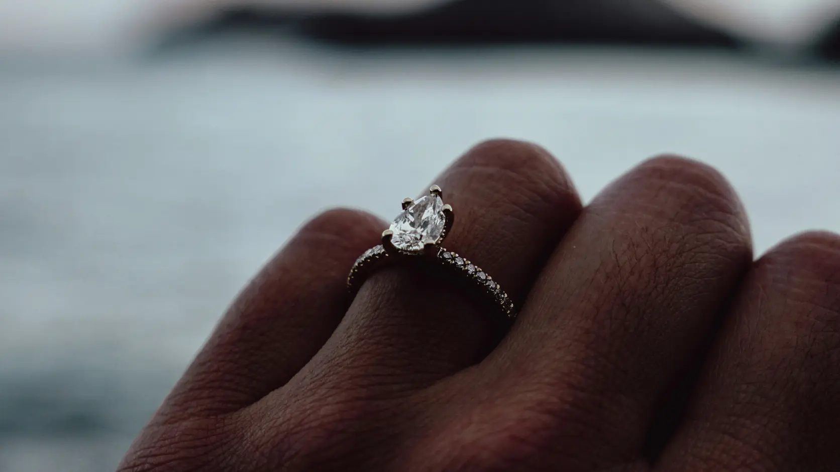 Anillo de compromiso con diamante brillante apoyado sobre una calculadora plateada en mármol gris oscuro, representando el contraste entre el lujo del anillo y la presión financiera del mito de los tres meses de sueldo