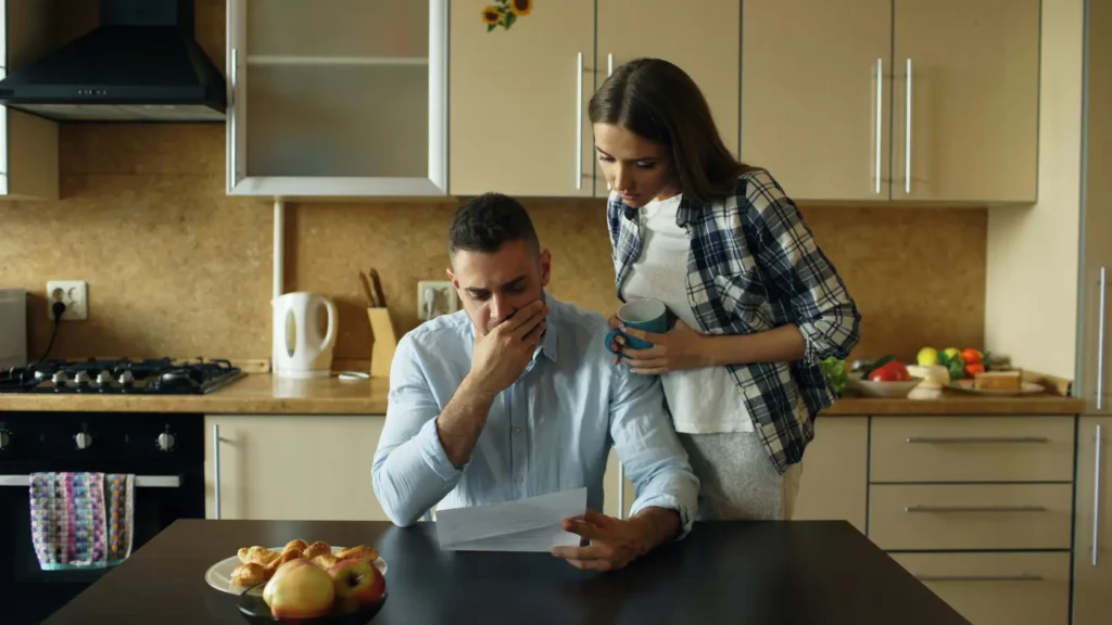 Pareja joven revisando facturas y documentos en casa con gesto de preocupación al descubrir un sobrecoste oculto del 35% en el presupuesto de su boda