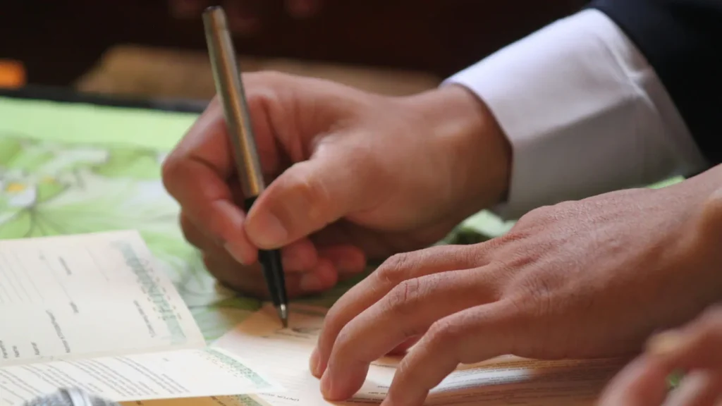 Contrato de préstamo bancario sobre una mesa junto a una alianza de boda y un bolígrafo, representando el coste real e intereses de financiar una boda en 2026 con un préstamo personal